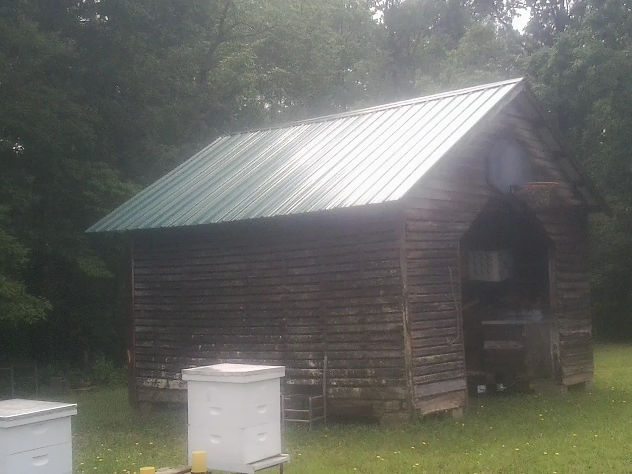 Green metal roof on a weathered barn beside stacked beehives in Dale