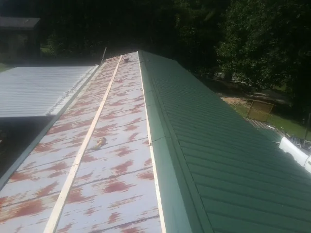 Old rusted panels beside newly installed green metal roofing — Wind Damage Roof Repair by Roofing Brothers in Dale